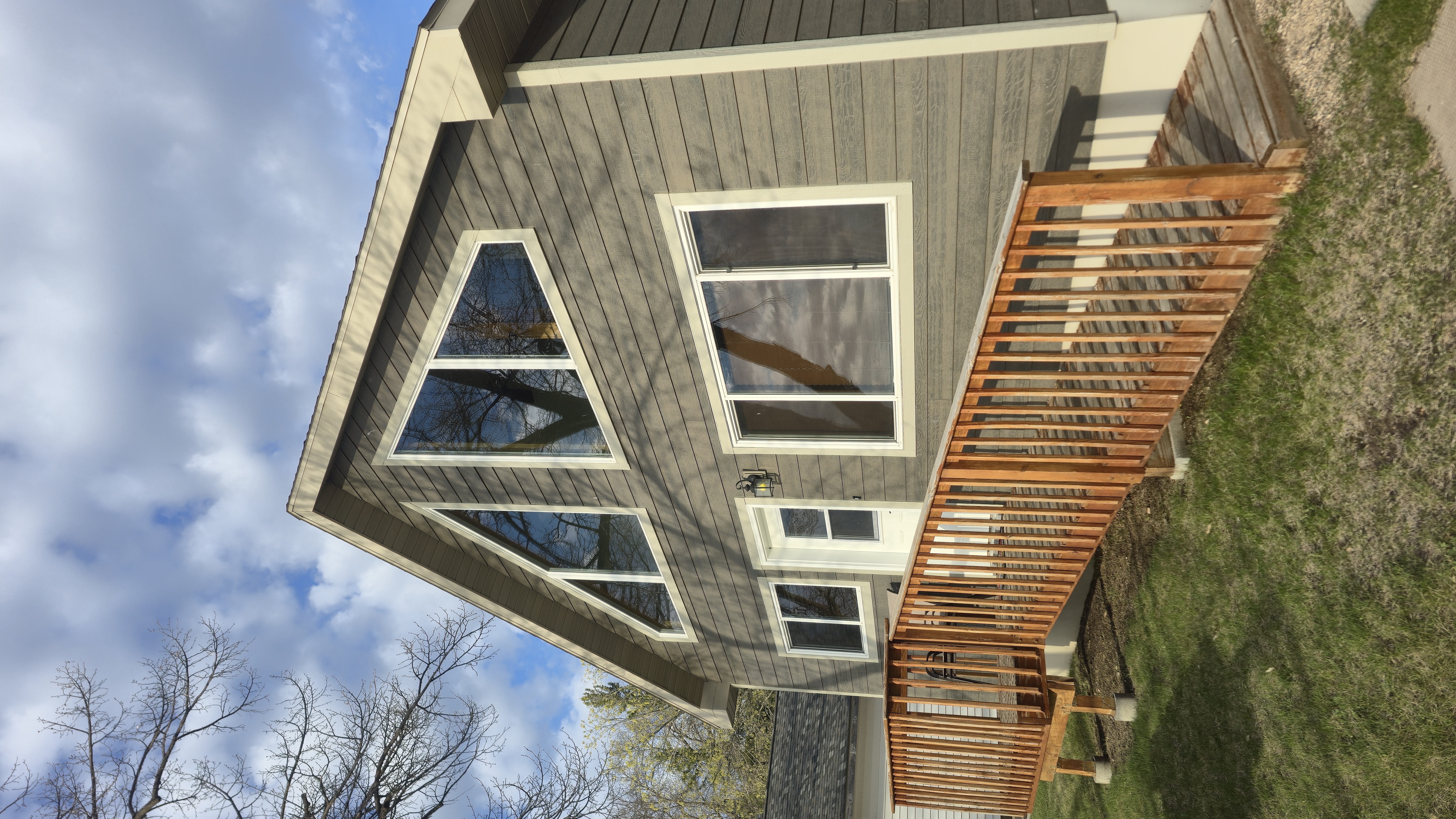 A modern house with a triangular roof, large windows, and a wooden deck.